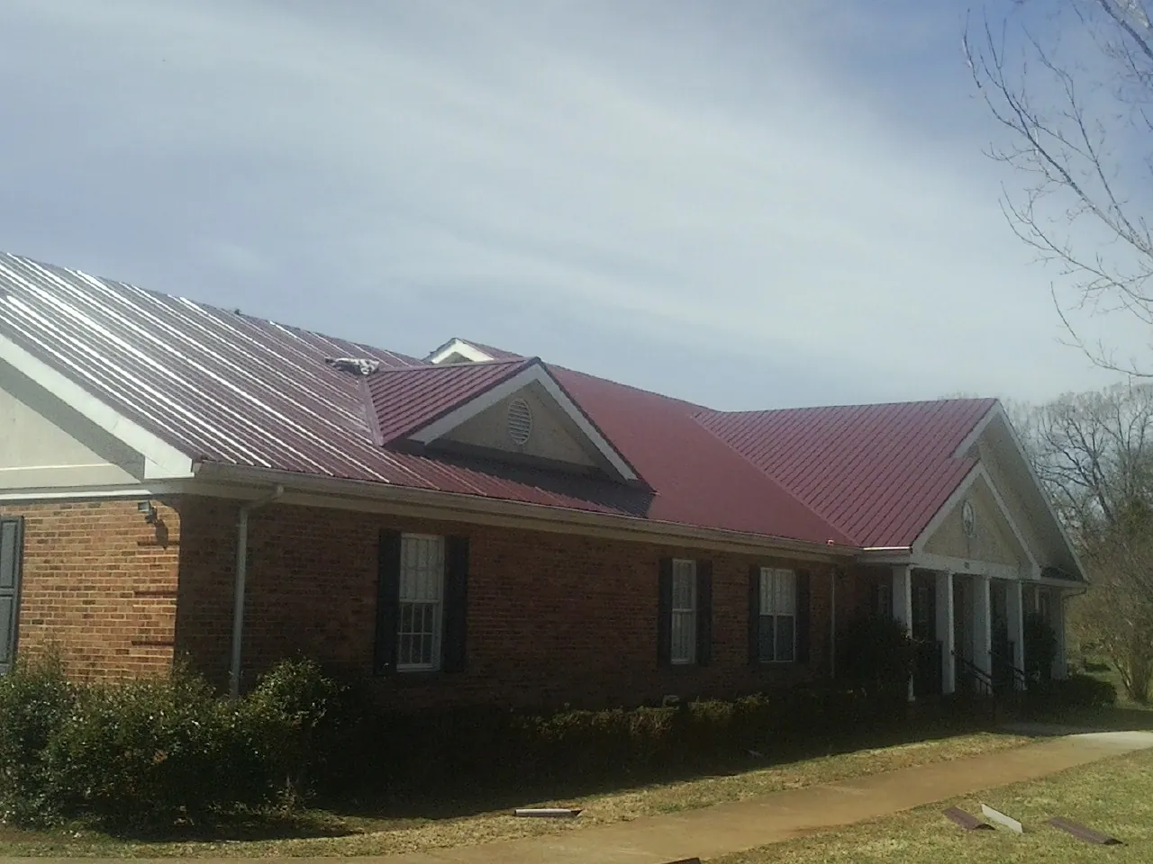 Red metal roof with gabled entries on a long brick building, from a Hail Damage Roof Repair job in Georgetown